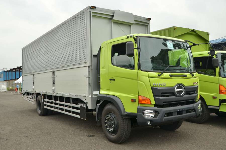 Armada truk Hino wingbox di gudang dengan muatan kardus dan aktivitas bongkar muat